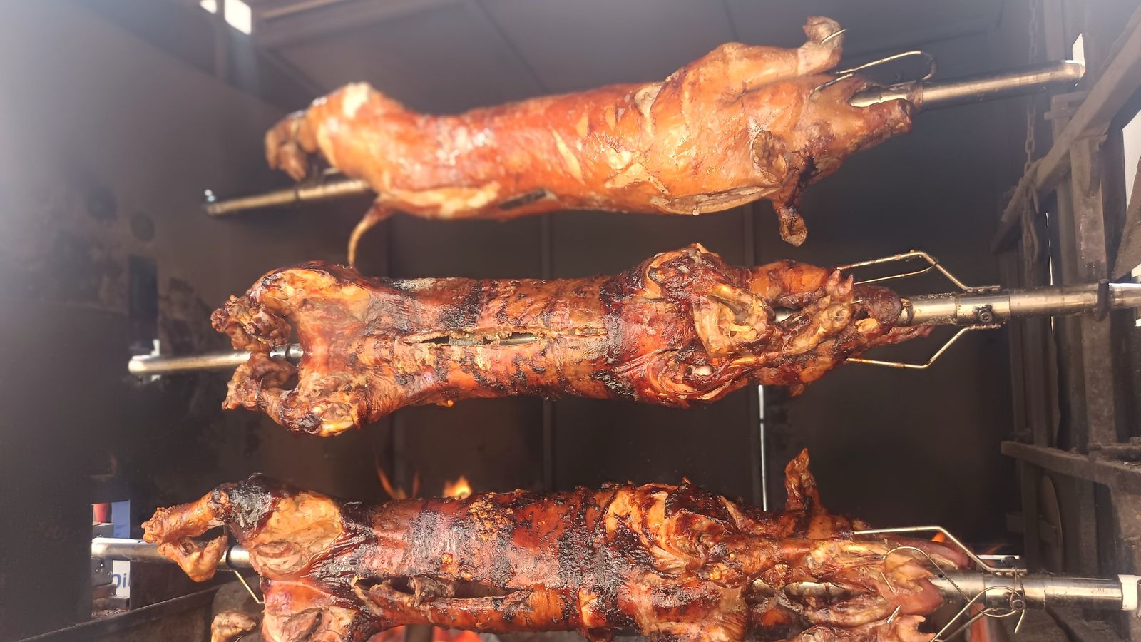 Drei Spieße mit Spanferkel und Lamm über offener Holzglut